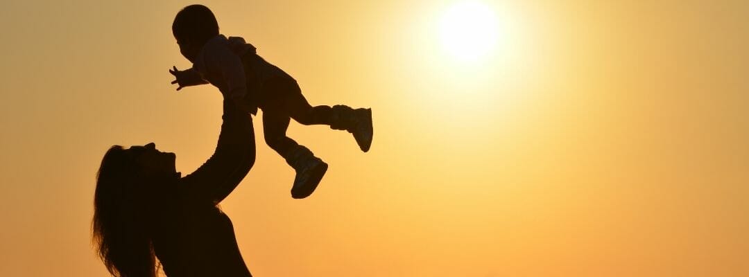 This is an image of a silhouetted mother swinging a young child above her head against a sunset