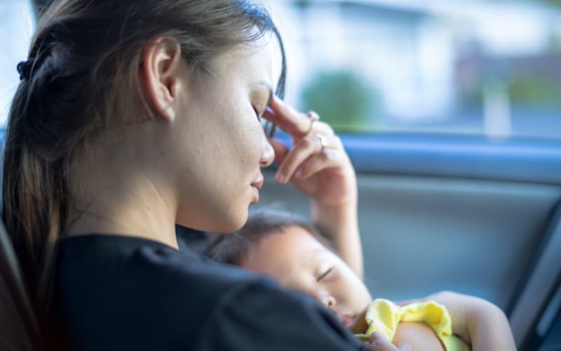 A woman embraces her baby in a car's back seat, highlighting the importance of community support for families in need from organisations like Women's Community Shelters.